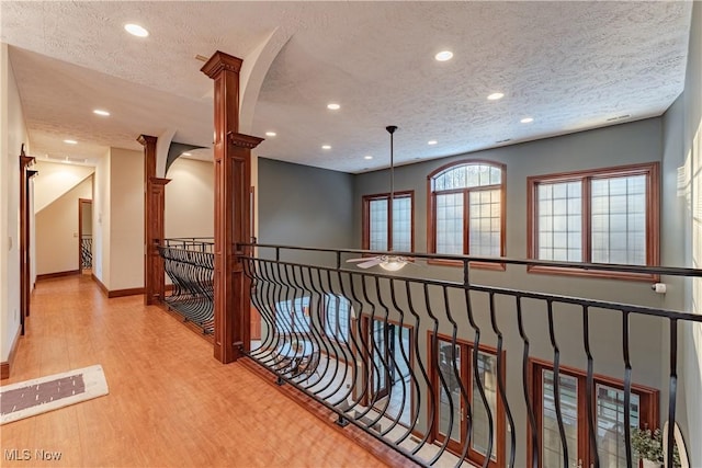 hall featuring decorative columns, a textured ceiling, and light hardwood / wood-style flooring