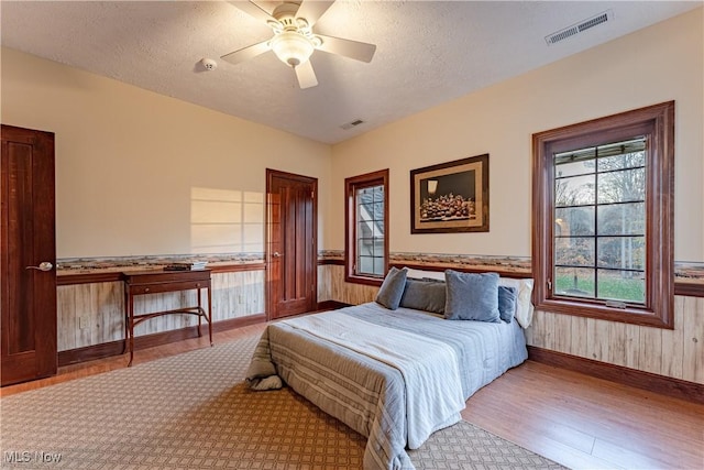 bedroom with ceiling fan, wooden walls, a textured ceiling, and light wood-type flooring