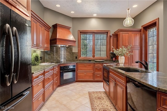 kitchen with premium range hood, dark stone counters, black appliances, sink, and decorative backsplash