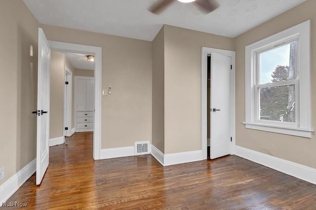 unfurnished bedroom with a textured ceiling, dark wood-type flooring, and ceiling fan