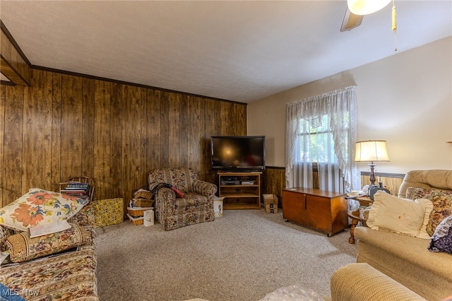 carpeted living room with ceiling fan, wooden walls, and crown molding