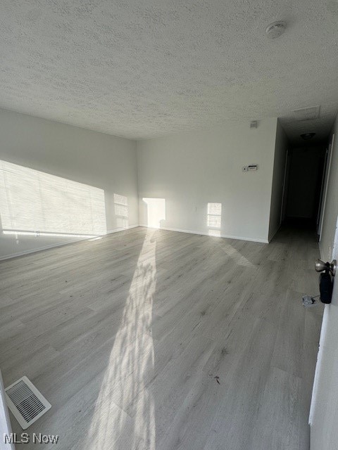 spare room featuring a textured ceiling, a healthy amount of sunlight, and light hardwood / wood-style flooring