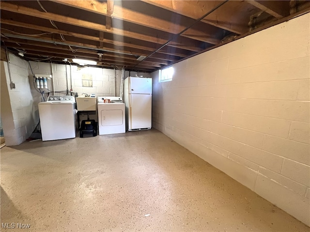 basement featuring sink, washer and clothes dryer, and white fridge