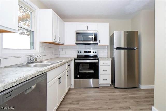 kitchen with white cabinets, sink, light hardwood / wood-style flooring, tasteful backsplash, and stainless steel appliances