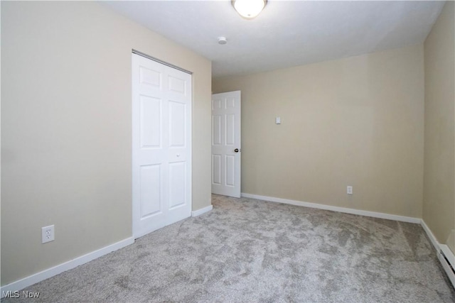 unfurnished bedroom featuring baseboard heating, a closet, and light colored carpet