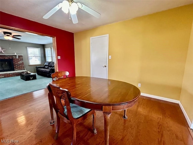 dining room featuring a brick fireplace, hardwood / wood-style floors, and ceiling fan