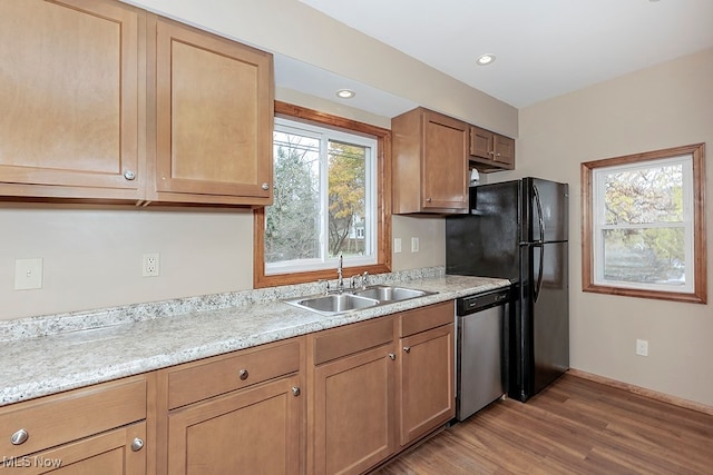 kitchen featuring light hardwood / wood-style floors, sink, light stone countertops, black refrigerator, and dishwasher