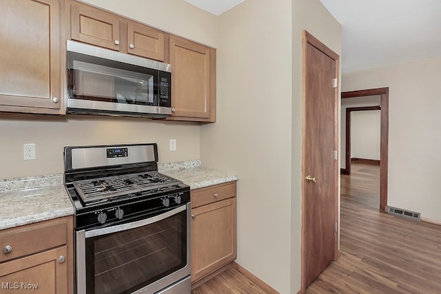 kitchen featuring stainless steel appliances, light hardwood / wood-style flooring, and light stone counters