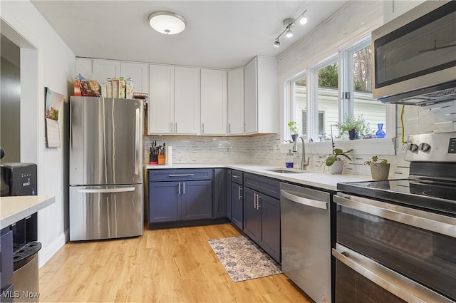 kitchen with stainless steel appliances, light hardwood / wood-style floors, blue cabinets, white cabinets, and tasteful backsplash