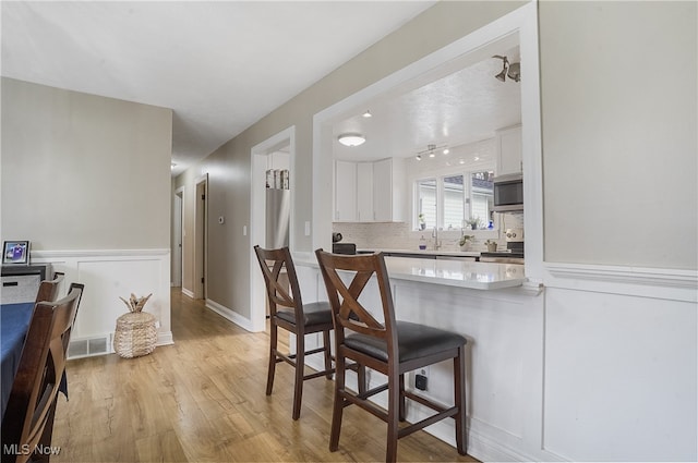 kitchen with light hardwood / wood-style floors, sink, tasteful backsplash, a kitchen bar, and white cabinets