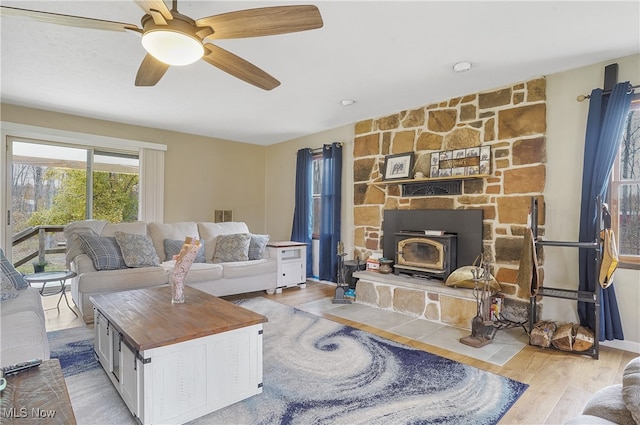 living room with a wood stove, light hardwood / wood-style floors, and ceiling fan