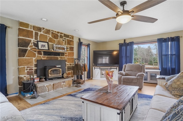 living room with a wood stove, light wood-type flooring, and ceiling fan