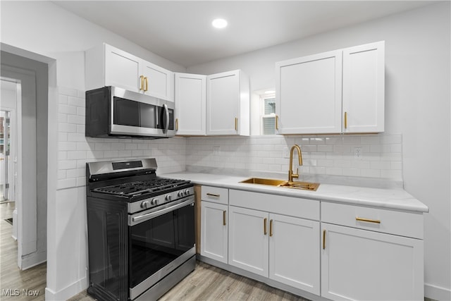 kitchen with stainless steel appliances, white cabinetry, sink, backsplash, and light wood-type flooring