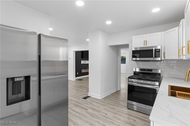 kitchen featuring tasteful backsplash, stainless steel appliances, light wood-type flooring, white cabinetry, and sink