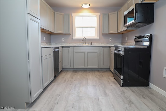 kitchen with light wood-type flooring, stainless steel appliances, sink, and gray cabinetry