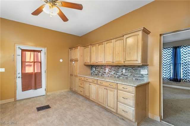 kitchen with backsplash, light stone countertops, light brown cabinets, and ceiling fan