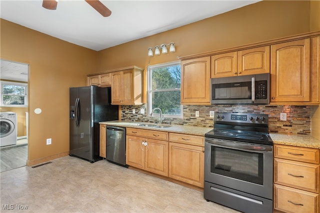 kitchen with black appliances, washer / dryer, light stone countertops, and sink