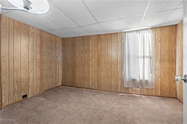 unfurnished room featuring carpet flooring, a drop ceiling, and wooden walls