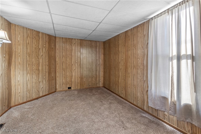 empty room with carpet flooring, a drop ceiling, and wooden walls