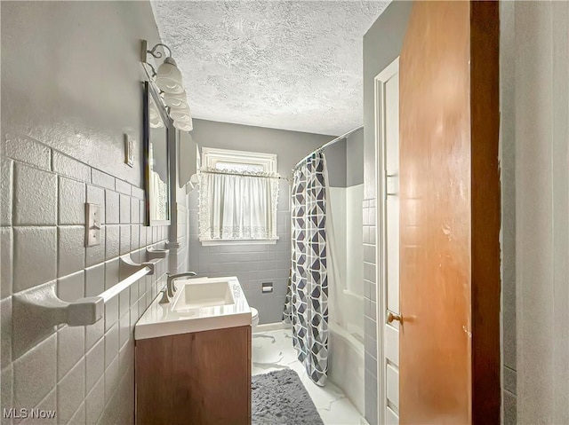 bathroom featuring a textured ceiling, shower / bath combo with shower curtain, vanity, and tile walls