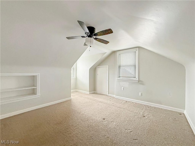 additional living space featuring lofted ceiling, ceiling fan, light colored carpet, and built in features