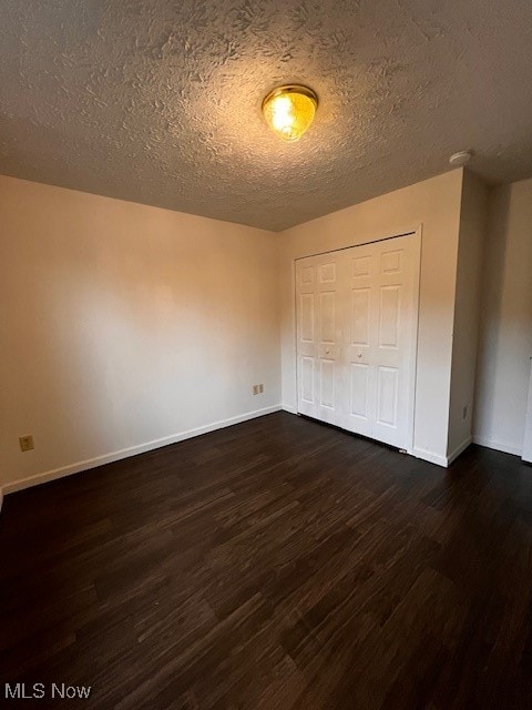 unfurnished bedroom with dark hardwood / wood-style flooring, a textured ceiling, and a closet