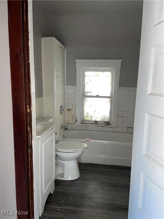 bathroom featuring lofted ceiling, toilet, hardwood / wood-style flooring, vanity, and a tub to relax in