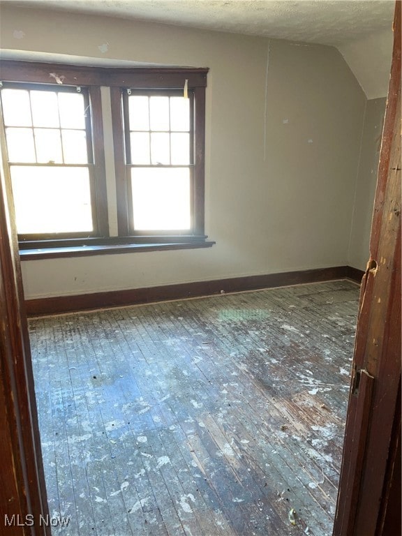 unfurnished room featuring hardwood / wood-style flooring, lofted ceiling, and a textured ceiling