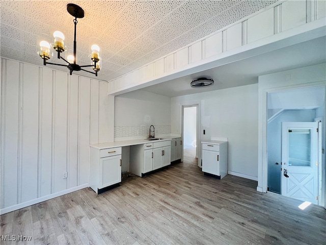 kitchen with white cabinetry, an inviting chandelier, hanging light fixtures, light wood-type flooring, and decorative backsplash