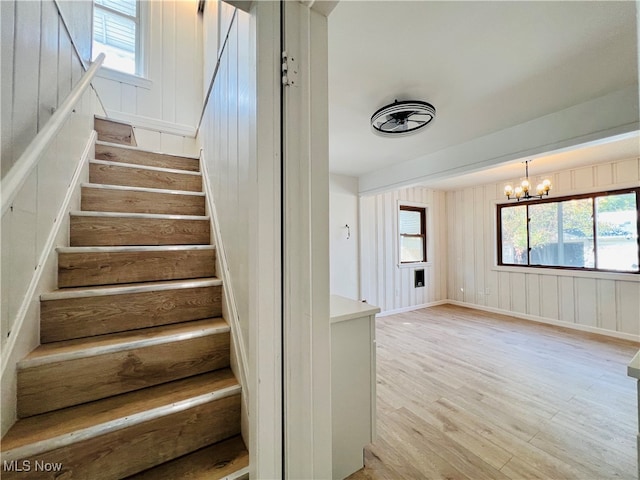 stairs with wooden walls, wood-type flooring, and a notable chandelier