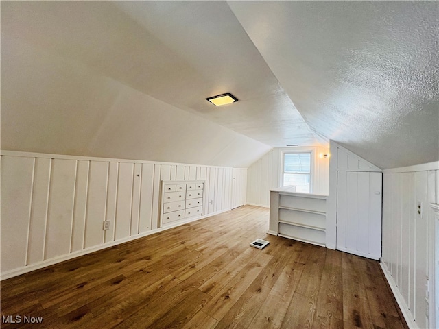 bonus room with hardwood / wood-style floors, lofted ceiling, and a textured ceiling