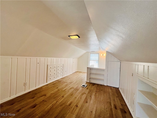 additional living space with hardwood / wood-style floors, vaulted ceiling, and a textured ceiling