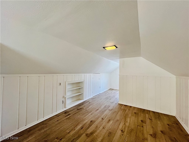 additional living space featuring hardwood / wood-style flooring, built in features, a textured ceiling, and lofted ceiling