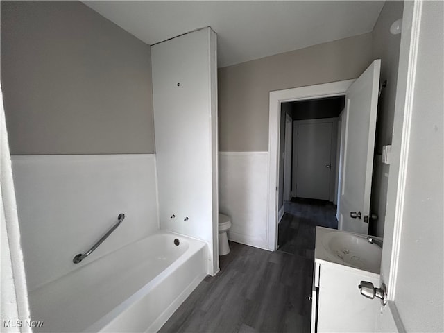 bathroom featuring toilet, vanity, hardwood / wood-style floors, and a tub