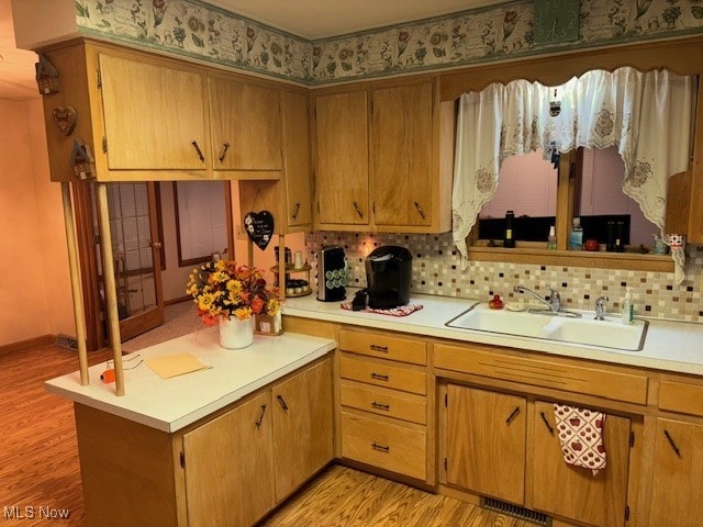 kitchen featuring light wood-type flooring, decorative backsplash, and sink