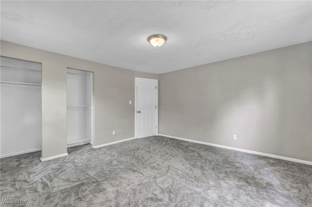 unfurnished bedroom featuring a textured ceiling, carpet flooring, and multiple closets