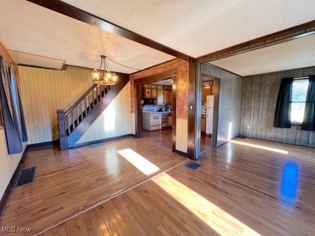 unfurnished living room with dark hardwood / wood-style flooring, wood walls, a chandelier, and beam ceiling