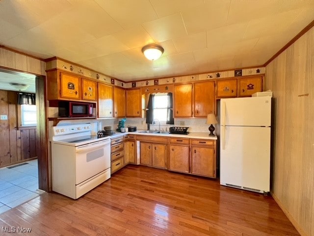 kitchen with wood walls, white appliances, sink, and light hardwood / wood-style flooring