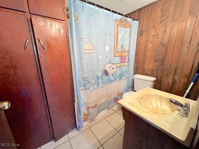 bathroom featuring a textured ceiling, curtained shower, vanity, tile patterned floors, and wooden walls