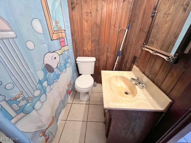 bathroom with tile patterned flooring, wood walls, toilet, and vanity