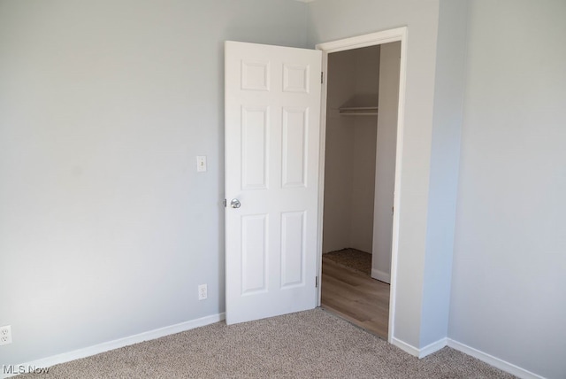 unfurnished bedroom featuring a closet, a walk in closet, and light colored carpet