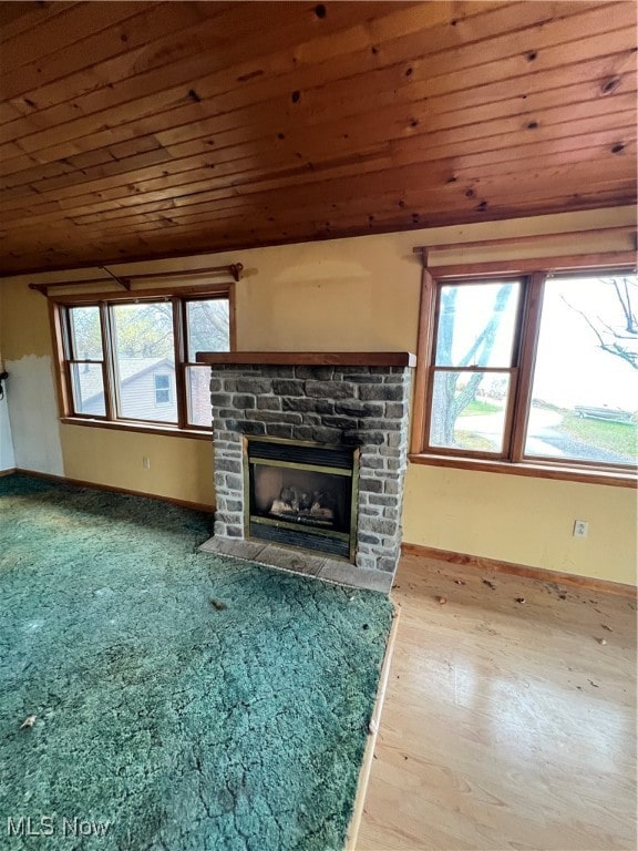 unfurnished living room featuring a stone fireplace, light wood-type flooring, wooden ceiling, and plenty of natural light