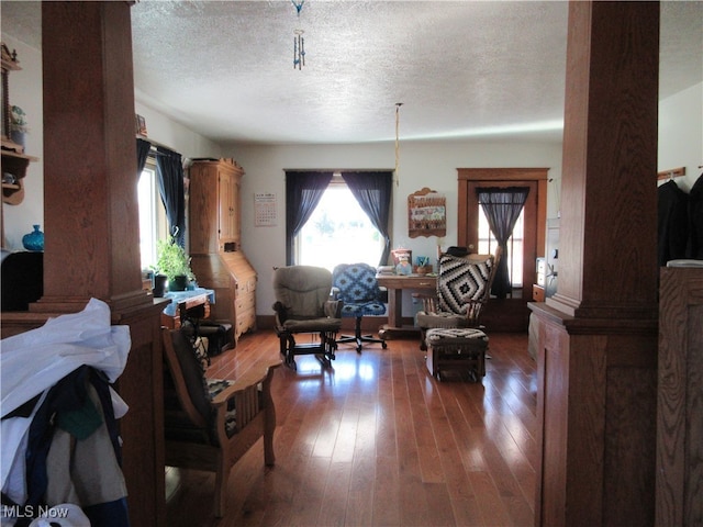 living room featuring dark hardwood / wood-style floors, a textured ceiling, and ornate columns