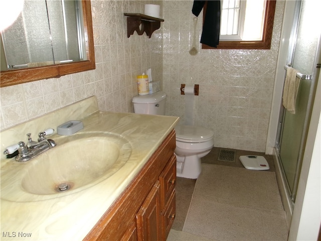 bathroom with tile walls, tile patterned floors, a shower with door, vanity, and toilet