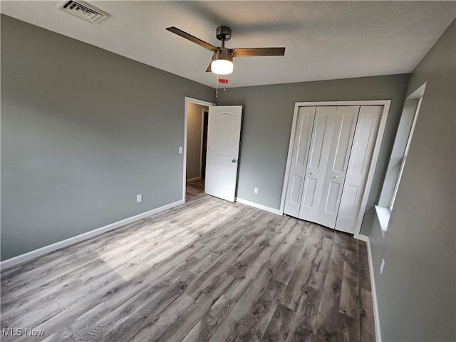 unfurnished bedroom featuring ceiling fan, light hardwood / wood-style floors, a textured ceiling, and a closet