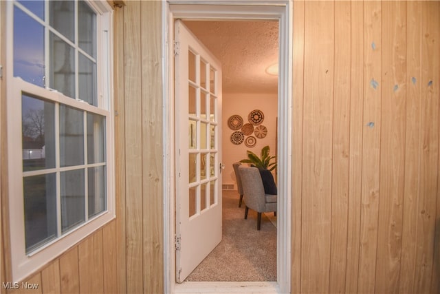 doorway featuring wood walls, a textured ceiling, and carpet floors