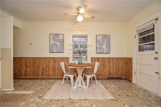 dining room featuring wood walls, ceiling fan, and a textured ceiling