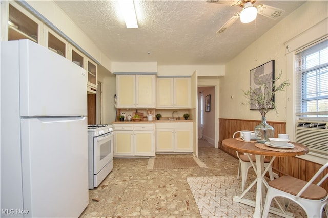 kitchen featuring a textured ceiling, wood walls, sink, white appliances, and ceiling fan