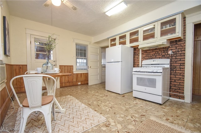 kitchen with white appliances, ceiling fan, a textured ceiling, and wooden walls