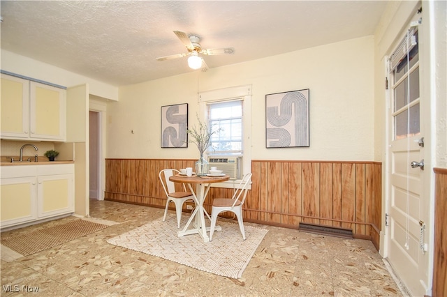 dining room with cooling unit, wood walls, a textured ceiling, sink, and ceiling fan